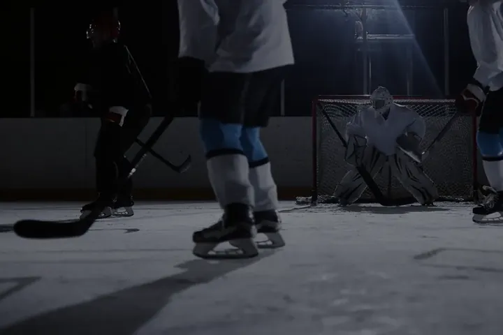 Hockey players and a goalie at the crease under rink lights